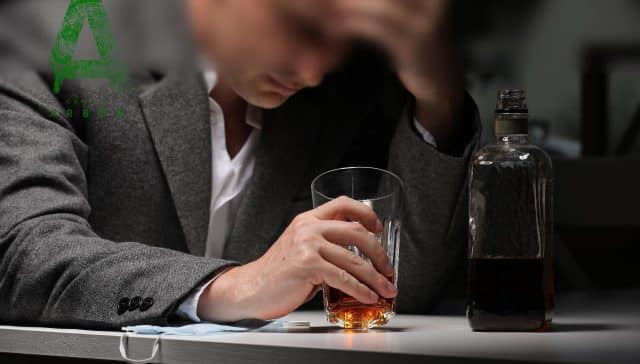Hombre con traje cabizbajo frente a un vaso de whisky y una botella de alcohol