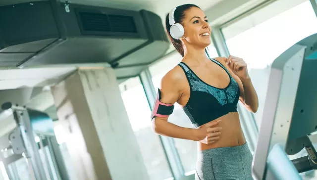 Mujer haciendo ejercicio en una cinta de correr con auriculares, sonriente y motivada.