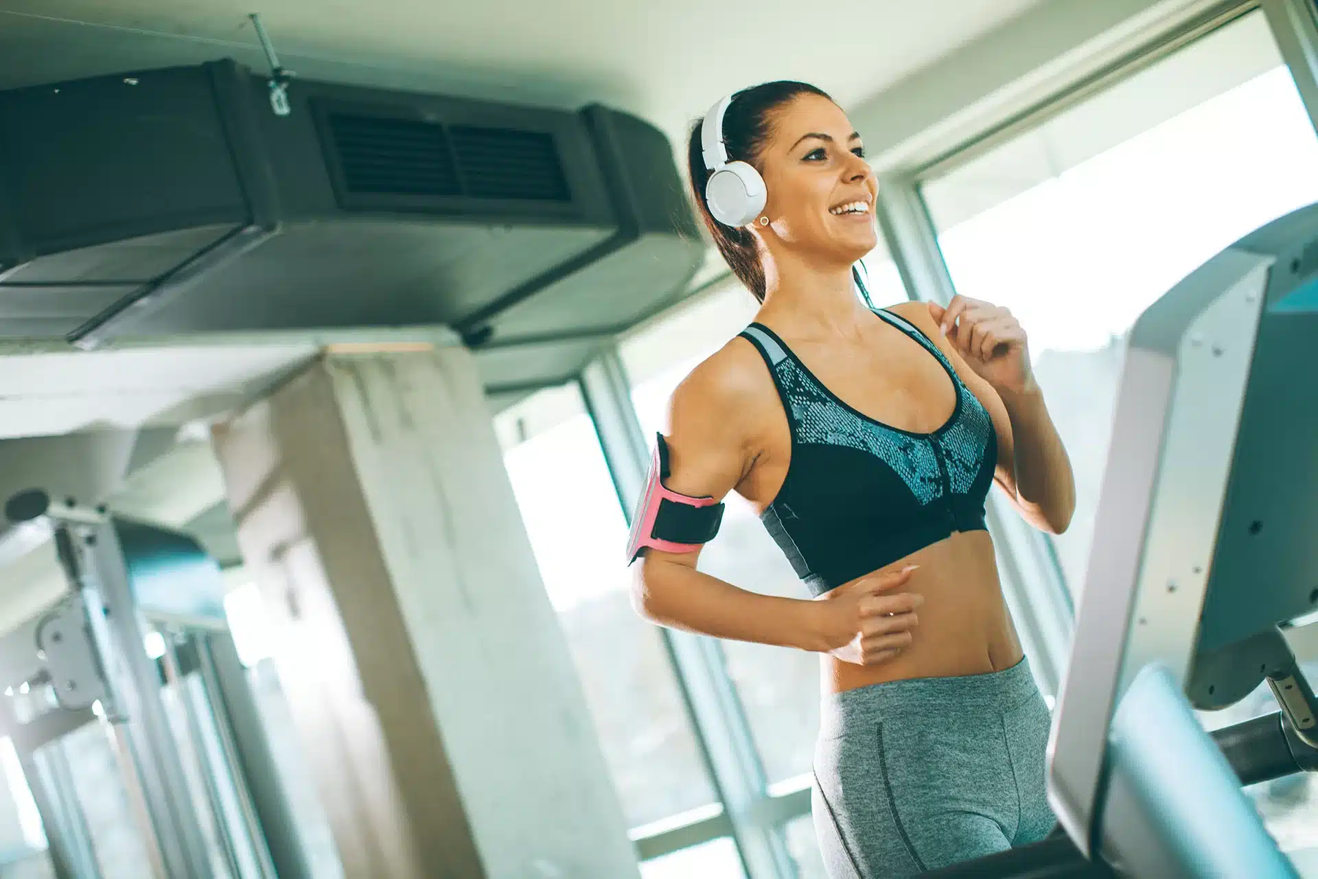Mujer haciendo ejercicio en una cinta de correr con auriculares, sonriente y motivada.