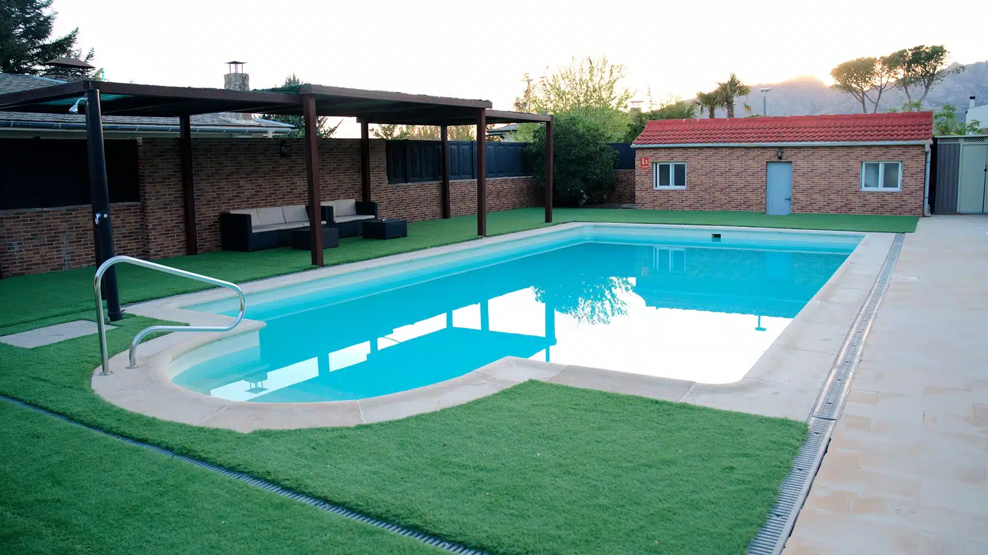 Espacio de calma y recuperación: piscina en el Centro Árbor (Soto del Real) Piscina con zona de sombra y sofás junto a edificio de ladrillo en el Centro de Desintoxicación Árbor en Madrid.