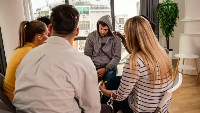 Sesión de terapia de grupo con personas compartiendo experiencias sobre el alcoholismo.
