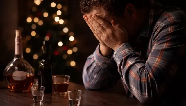 Hombre sentado solo con botellas de alcohol, mostrando angustia emocional durante el periodo navideño.