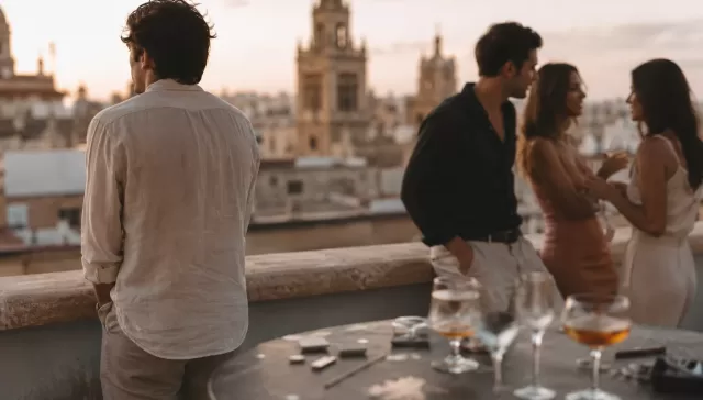Grupo de jóvenes consumiendo alcohol en una terraza durante el verano, mientras uno de ellos permanece apartado del grupo.