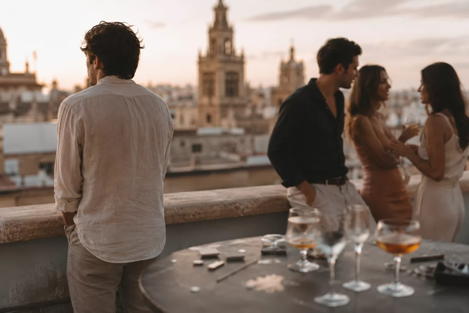 Grupo de jóvenes consumiendo alcohol en una terraza durante el verano, mientras uno de ellos permanece apartado del grupo.
